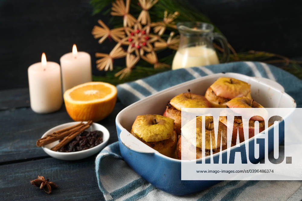 German baked apples filled with almonds, marzipan and honey in a casserole, ingredients, candles, and Christmas decoration against a dark blue background, festive holiday dessert, selected focus German baked apples filled with almonds, marzipan and honey in a casserole, ingredients, candles, and Christmas decoration against a dark blue background, festive holiday dessert, selected focus