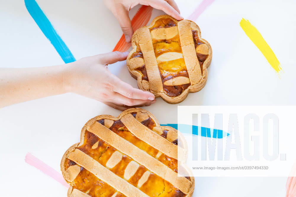 Cropped unrecognizable hands arranging Italian Easter pastiera napoletana pastries on a white surface with colorful brushstrokes. Model Released VictorCuenca_ID18923_563580_012