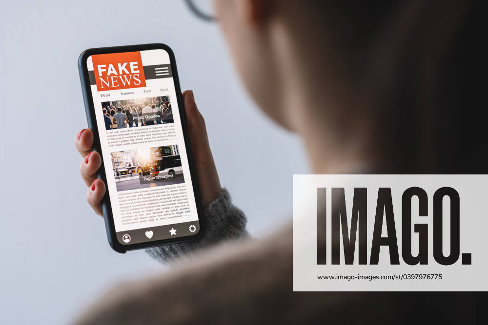 Online fake news on a mobile phone. Close up of woman reading Fake news HOAX or articles in a smartphone screen application. Hand holding smart device. Mockup website. Fake Newspaper portal. Online fake news on a mobile phone. Close up of woman reading Fake news HOAX or articles in a smartphone screen application. Hand holding smart device. Mockup website. Fake Newspaper portal. ,model released, Symbolfoto