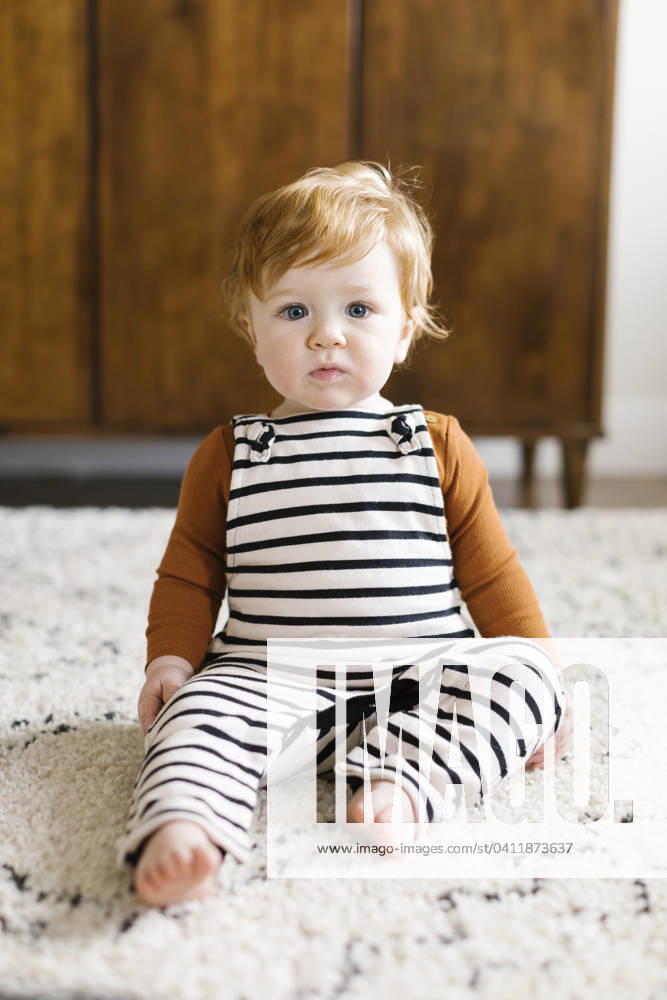 Baby boy wearing striped overalls , 22.03.2019, model released, TTBB_ti0061_05115.jpg, Color Image, Vertical, Front View, Selective Focus, Indoors, Day, One Person, People, 12-17 Months, Baby, Baby Boys, One Baby Boy Only, Only Baby Boys, Babies Only, Caucasian Appearance, Redhead, Home Interior, Living Room, Looking At Camera, Barefoot, Sitting, Overalls, Striped, Rug