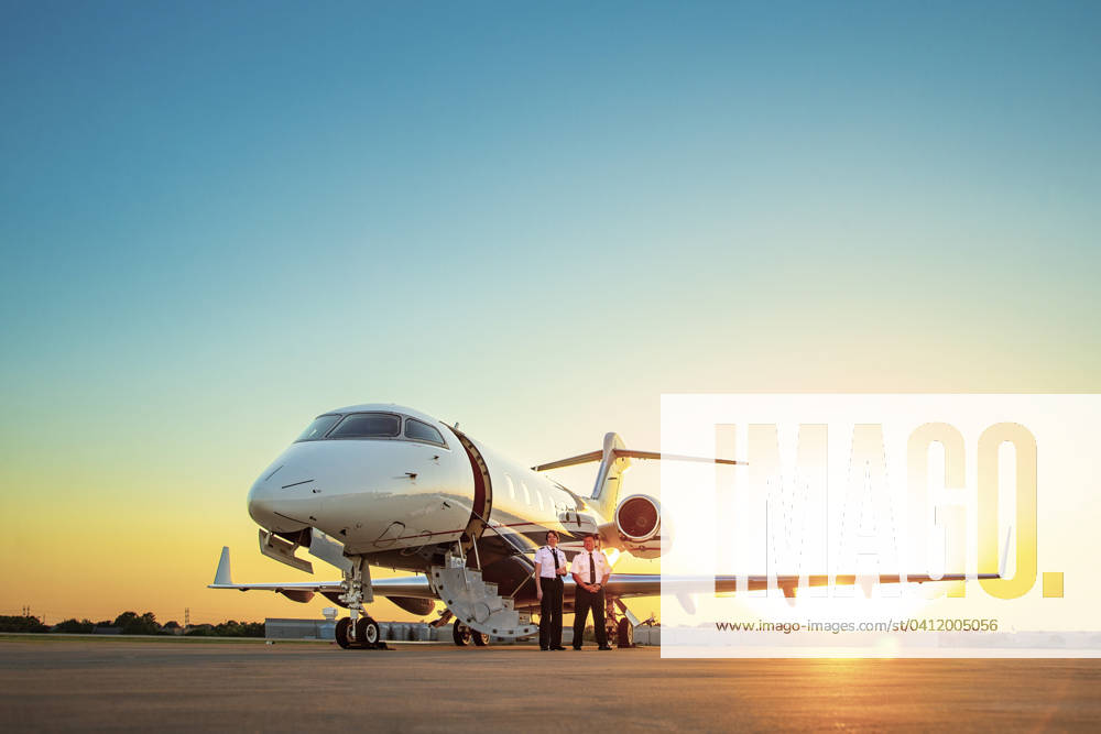 Two Pilots, One Female and one male, standing next to Jet on tarmac of small airport at sunset Addison Texas USA