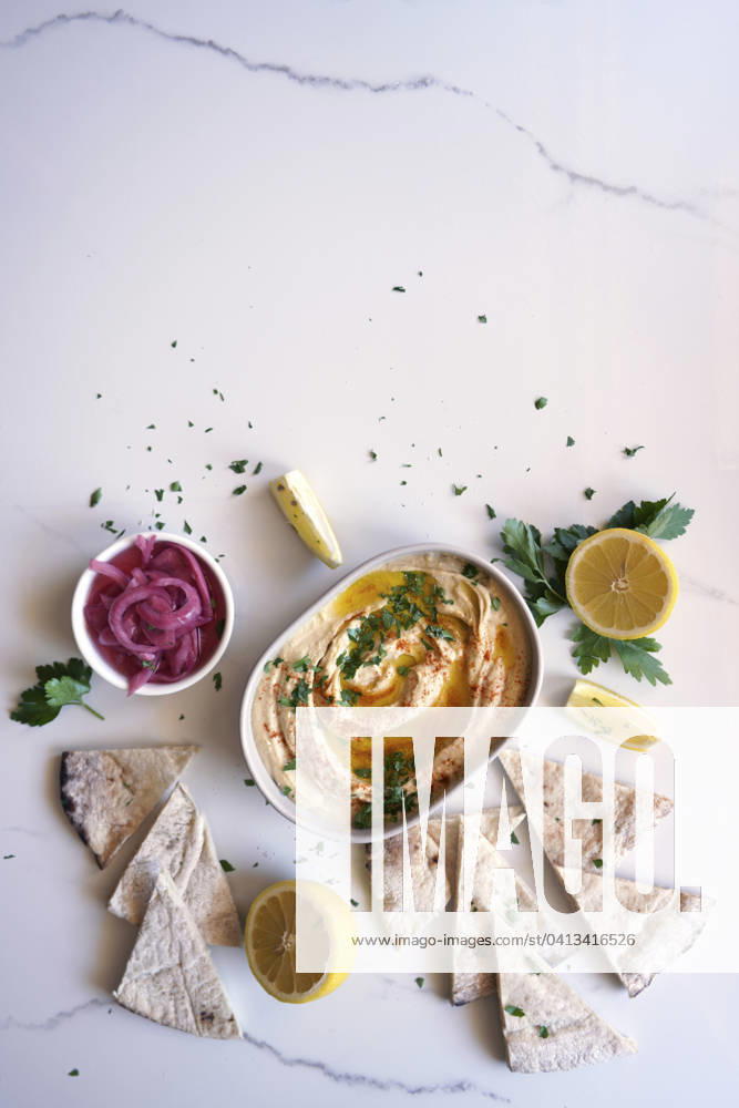 Chickpea hummus served with olive oil, pickled red onion, lemons, and flatbread on a white marble table background, with negative copy space. Chickpea hummus served with olive oil, pickled red onion, lemons, and flatbread on a white marble table background, with negative copy space.