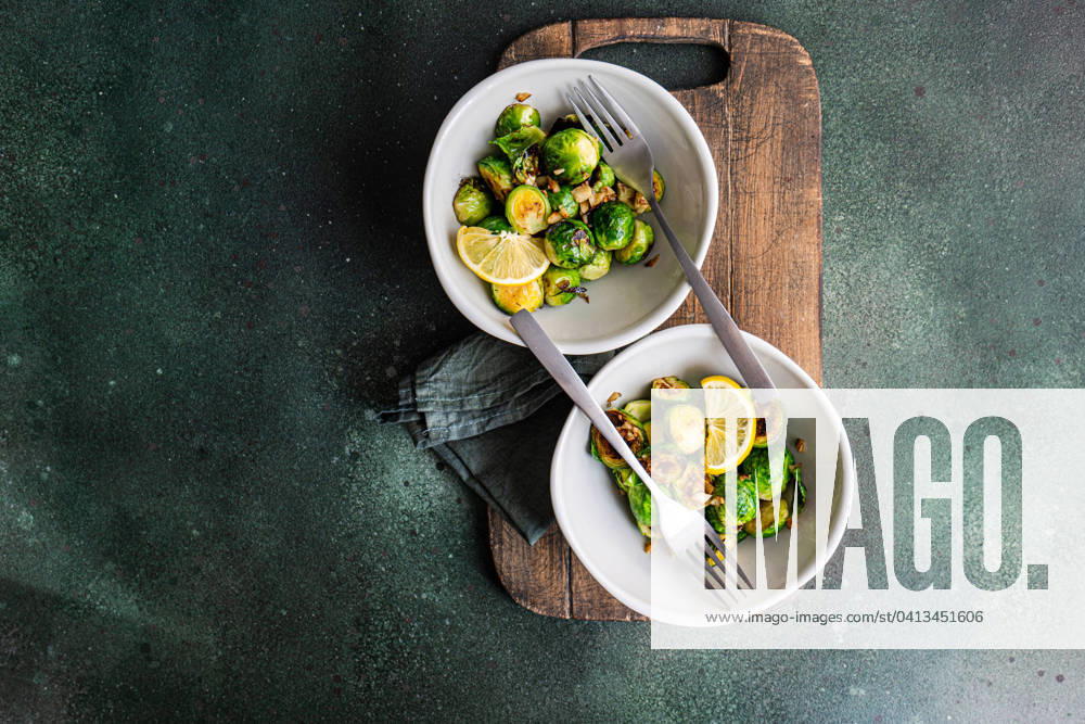 Top view of bowl of grilled Brussels sprouts seasoned with garlic and spices, garnished with a slice of lemon, served on a wooden board with a fork Model Released AnnaBogush_ID19160_569961_004