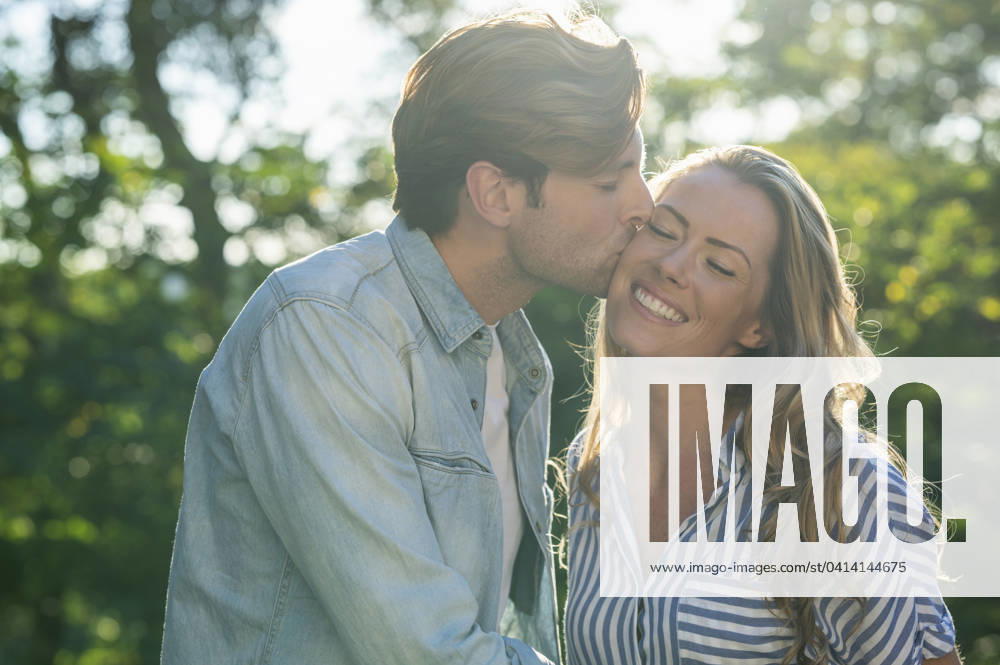 Adult man kissing girlfriend on the cheek while standing outdoors