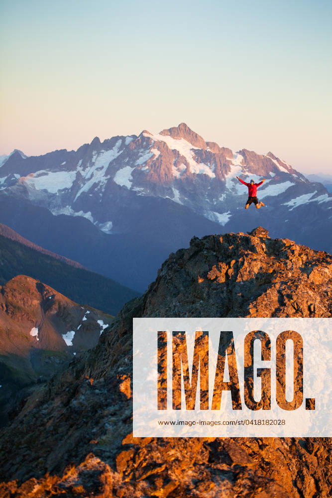 A hiker jumps off rocky cliff in North Cascades National Park. Glacier, Washington, United States CR_JDIP240227-1346434-01 ,model released, Symbolfoto