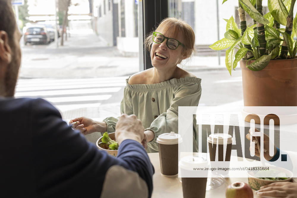 Cheerful businesswoman sharing lunch with colleague in cafeteria at workplace model released, Symbolfoto property released, JCCMF11199