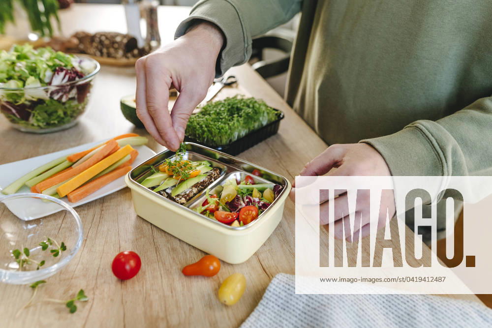 IMAGO Creative, Food, Trend, Meal Prep Man garnishing microgreen over vegetarian food in lunch box model released, Symbolfoto property released, YTF01683