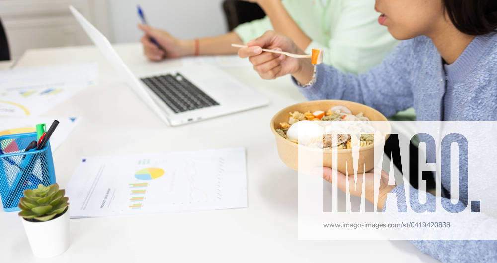 A person enjoys a healthy bowl of noodles with vegetables and egg during a busy workday, promoting productivity and well-being. Model Released DavidMunoz_ID19491_576509_063