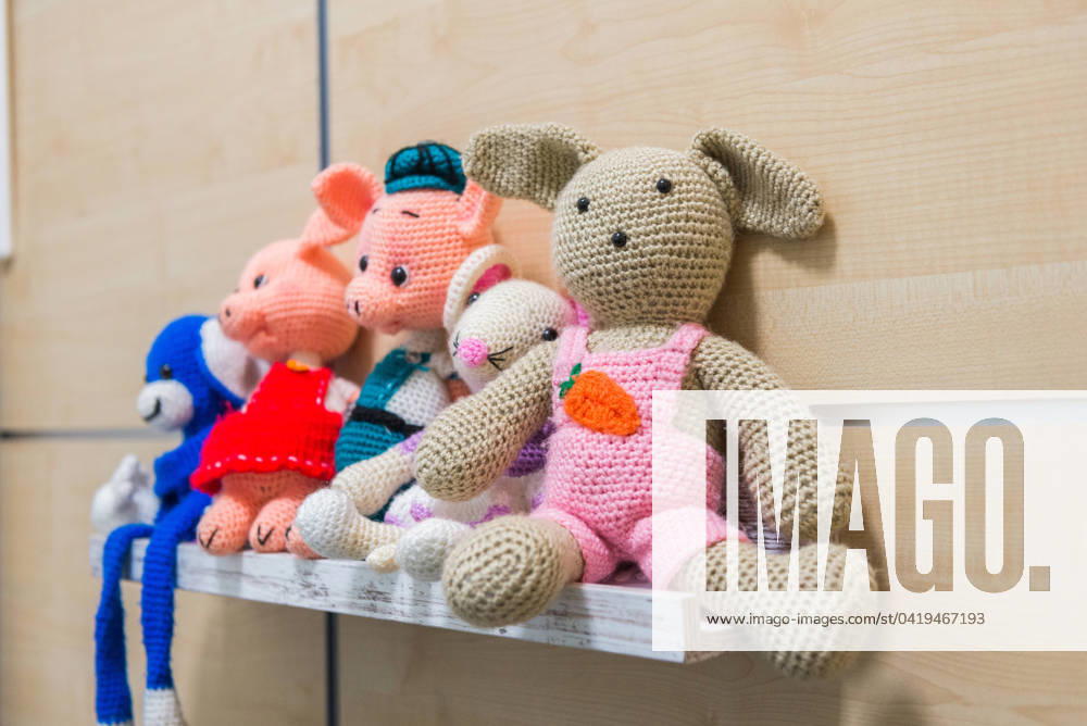 A collection of colorful handmade crochet stuffed toys, including animals, lined up on a wooden shelf against a neutral background Model Released NataliaPenado_ID19743_585601_005