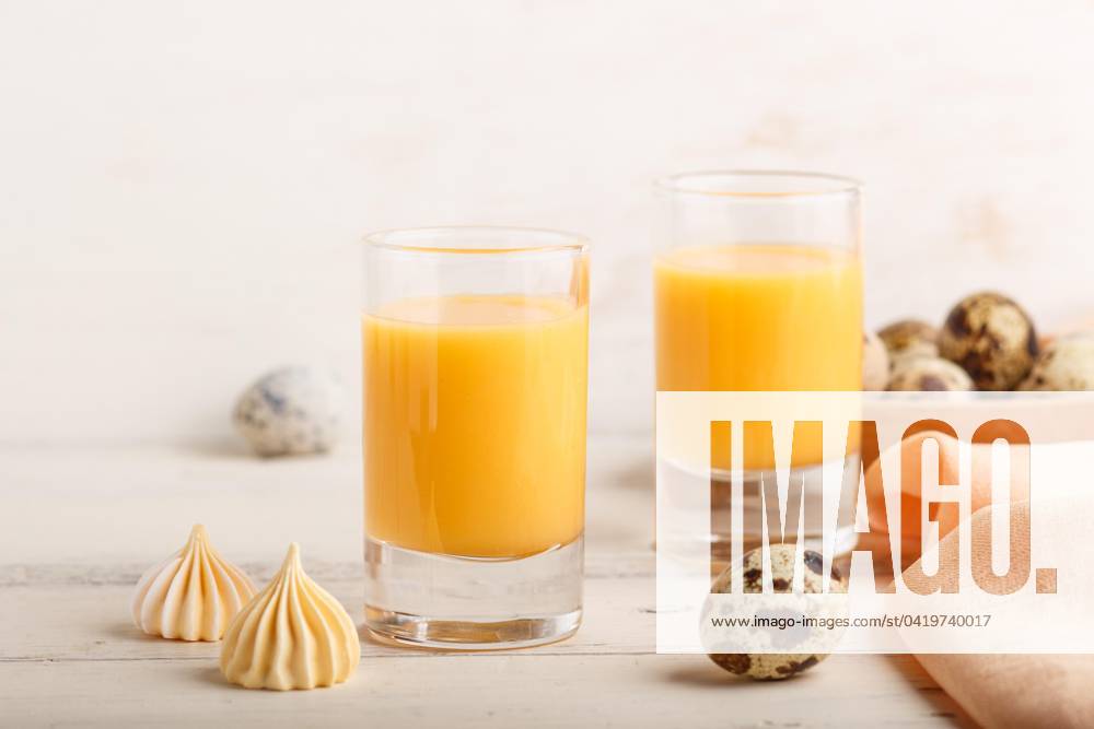 Sweetie Egg liqueur at Glass with Quail eggs and Meringues at white wood background Side view, Close-up, High Key