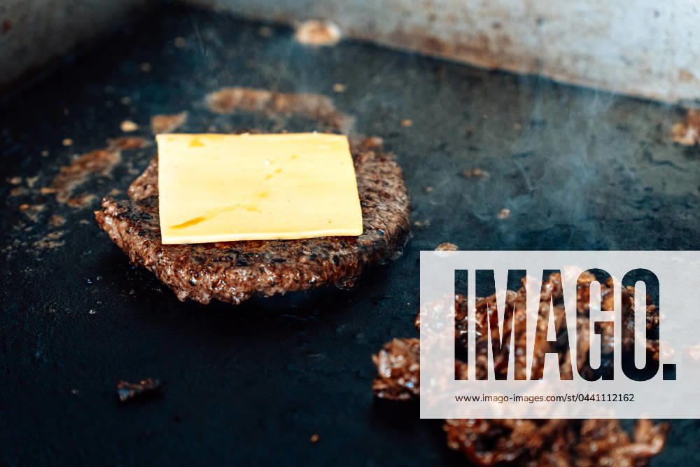 Preparation of a Philly cheese burger on a hot grill, meat and burger patty are seared with cheese