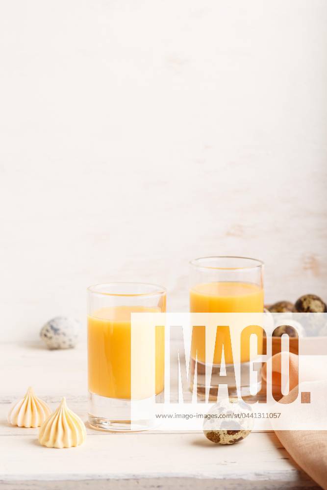 Sweetie Egg liqueur at Glass with Quail eggs and Meringues at white wood background Side view, Copy room, High Key, vertical