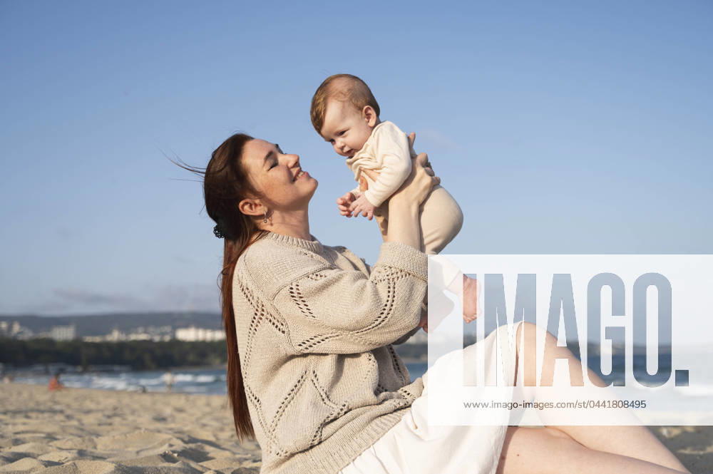 Smiling woman sitting on sand and playing with baby girl at beach model released, Symbolfoto, ALKF00994