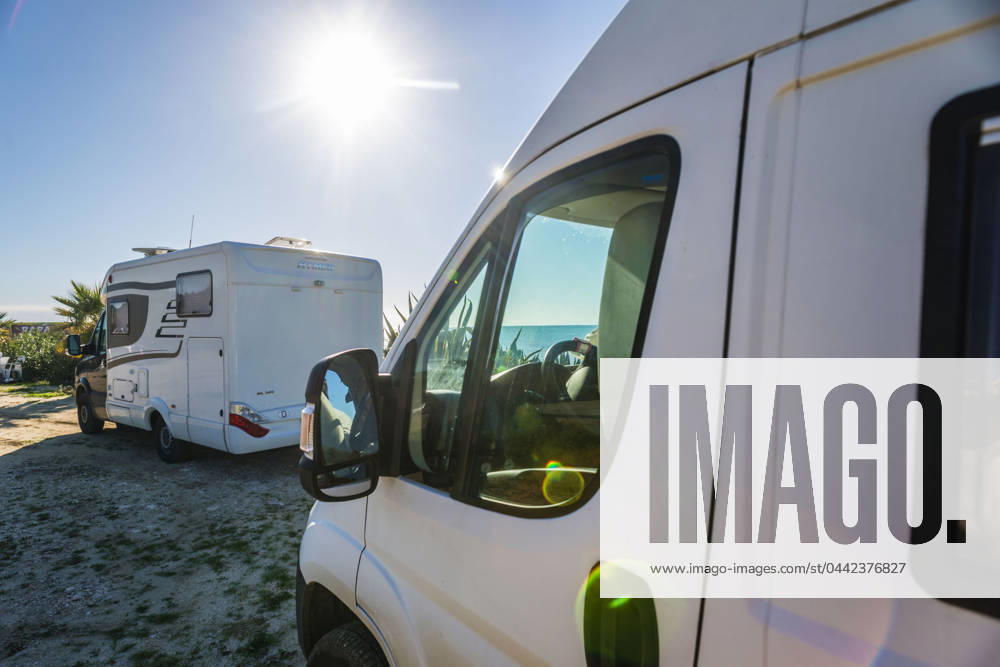 A camper van and an alcove motorhome are parked on a pitch on the unpaved shore on the Mediterranean coast in Sicily, Italy A camper van is parked on a pitch on the shore of the Mediterranean Sea