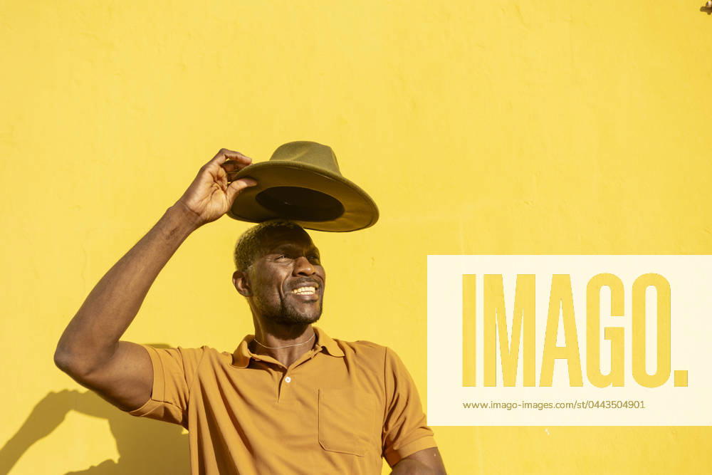 A cheerful African man tipping his hat with a sunny yellow background, evoking warmth and happiness Model Released JuanAizpuru_ID20348_601907_036