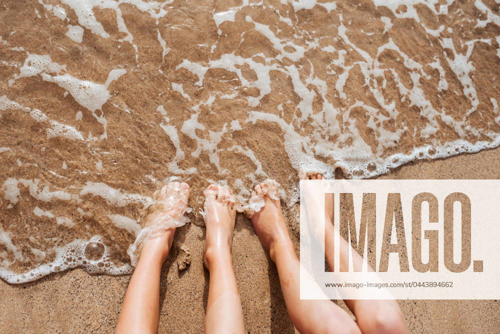 Close up of feet on beach with sea water beneath them. Sea foam and warm water soaking legs. Close up of feet on beach with sea water beneath. Sea foam and warm water soaking legs. model released
