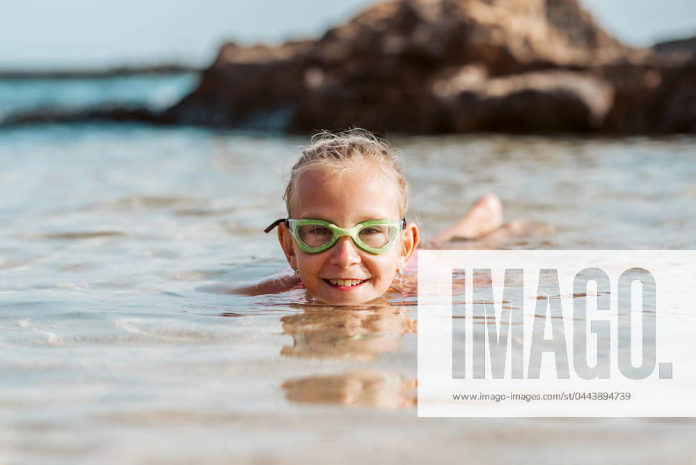 Young girl playing, swiming and splashing in fresh sea water. Smilling blonde girl in swimsuit with and swimming goggles. Concept of beach summer vacation with kids. Young girl on the beach. Smilling blonde girl enjoying sandy beach, looking at crystalline sea in Canary Islands. Concept of beach summer vacation with kids. model released