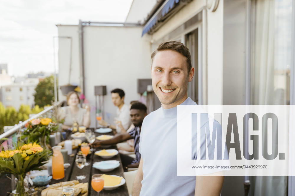 Portrait of smiling man with multiracial friends celebrating during dinner party in balcony Germany, Berlin, model released, property released