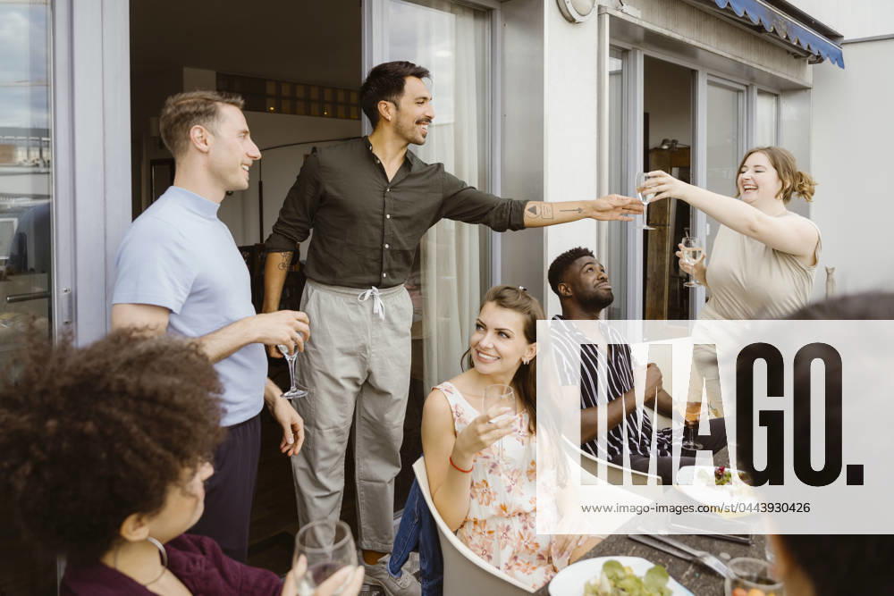 Smiling woman passing wineglass to male friend at dinner party in balcony Germany, Berlin, model released, property released