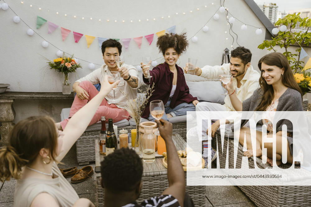 Group of multiracial friends toasting drinks while sitting together in balcony Germany, Berlin, model released, property released