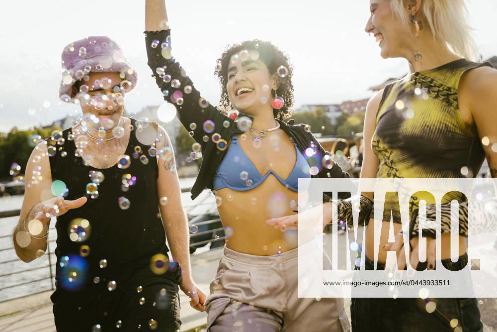 Carefree non-binary friends playing with bubbles on promenade in city Germany, Berlin, model released