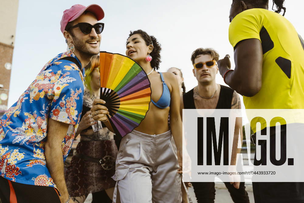 Non-binary person holding hand fan and dancing with multiracial friends in city Germany, Berlin, model released