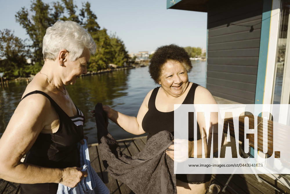 Happy senior female friends holding towel while standing on houseboat at sunny day Germany, Berlin, model released, property released