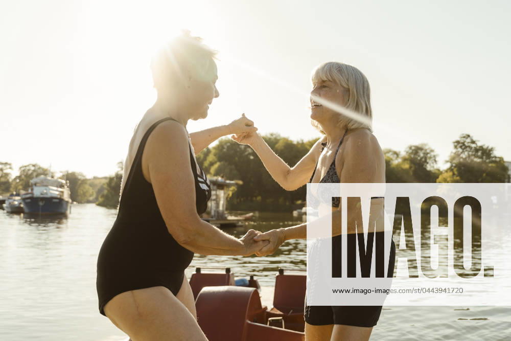 Happy senior female friends holding hands and dancing on houseboat during vacation Germany, Berlin, model released, property released