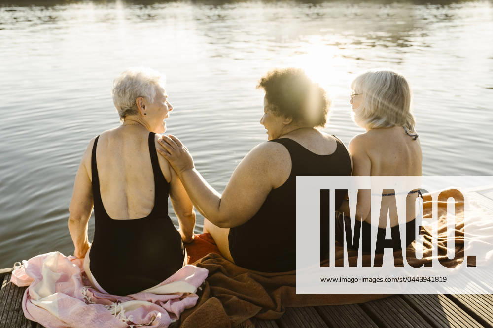 Happy elderly female friends talking while sitting on houseboat near lake on vacation Germany, Berlin, model released, property released