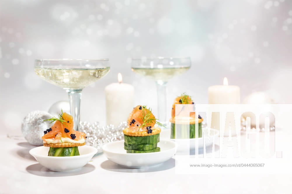 Festive canapes from smoked salmon, cucumber, crackers and caviar, in the background gasses with champagne, candles and decoration, holiday snack for Christmas or new year, copy space Festive canapes from smoked salmon, cucumber, crackers and caviar, in the background gasses with champagne, candles and decoration, holiday snack for Christmas or new year, copy space, selected focus