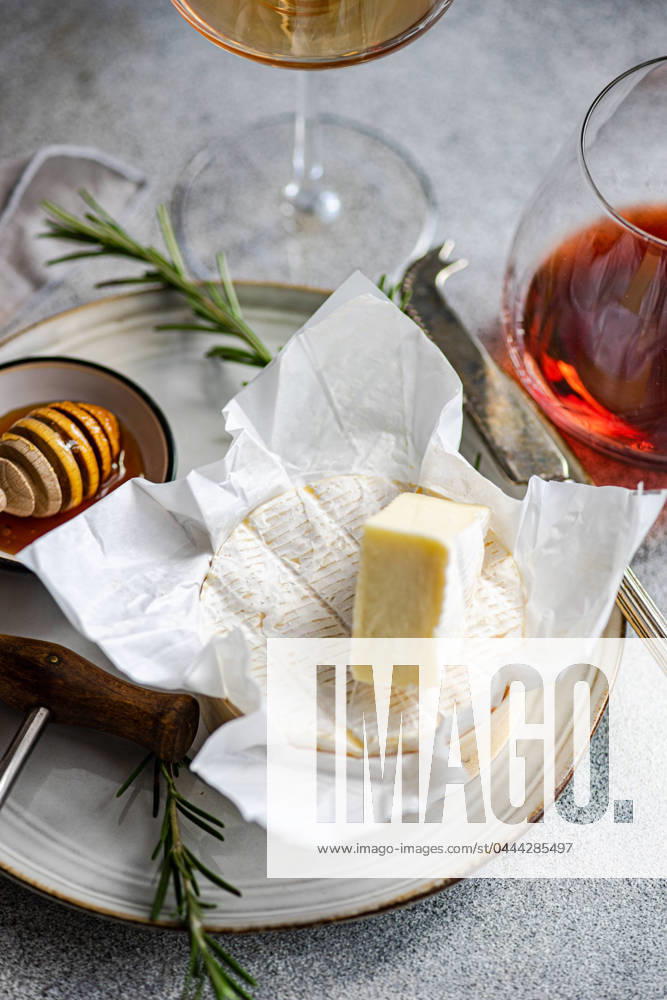 An elegant presentation of brie cheese with honeycomb, rosemary, and wine glasses on a textured surface for sophisticated dining. Model Released AnnaBogush_ID20594_608291_009