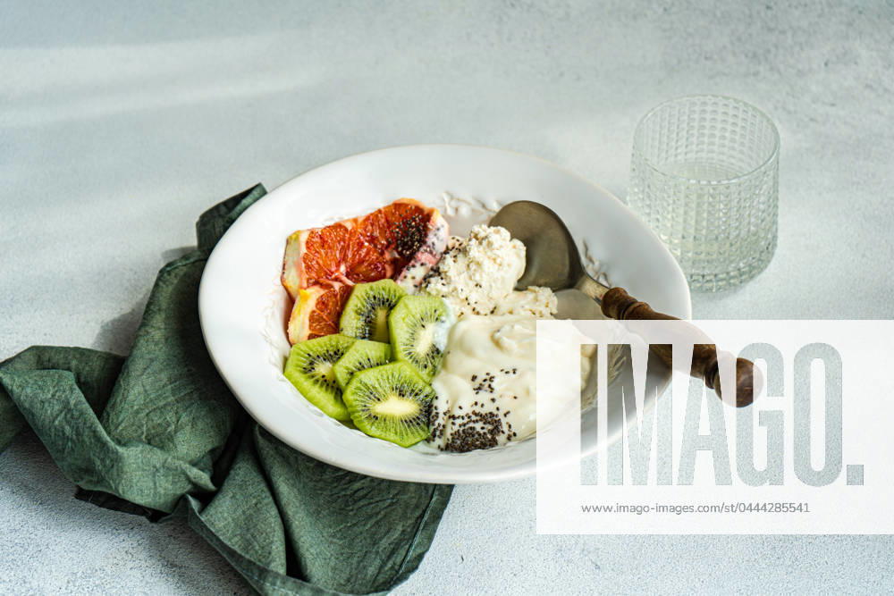 A well-balanced breakfast setting featuring a white bowl with cottage cheese, natural yogurt, and chia seeds, accompanied by kiwi and Sicilian orange slices Model Released AnnaBogush_ID20662_610159_010