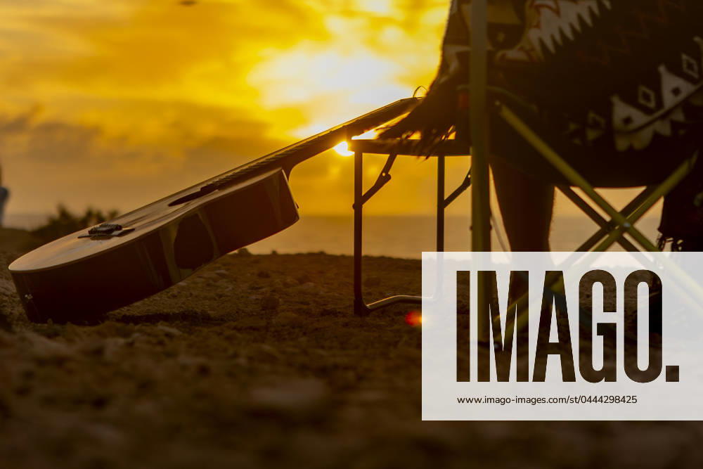 Back view of crop unrecognizable nomadic musician s guitar resting at a beachside campsite during a golden sunset, symbolizing inspiration and wanderlust. Model Released JuanAizpuru_ID20562_607331_033