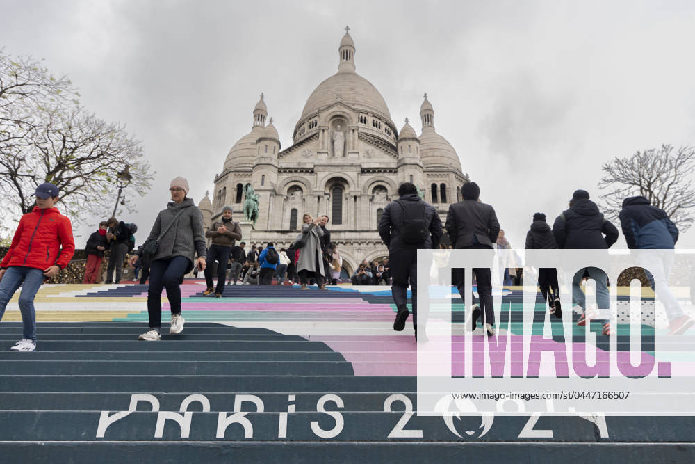 Paris, France April 19, 2024 - People walk up the stairs leading to the Sacre Coeur basilica decorated with a fresco in Olympic colors as part of the preparations for the Paris 2024 Olympic Games. Less than 100 days remain for the Olympic and Paralympic Games organizers to finalize preparations for the event that will welcome millions of visitors from July 16. OLY, JEUX OLYMPIQUES PARIS 2024, DECORATIONS, FRESQUE, ILLUSTRATION, MONTMARTRE, BASILIQUE DU SACRE COEUR, SPORT, ESCALIERS, MARCHES COLOREES,