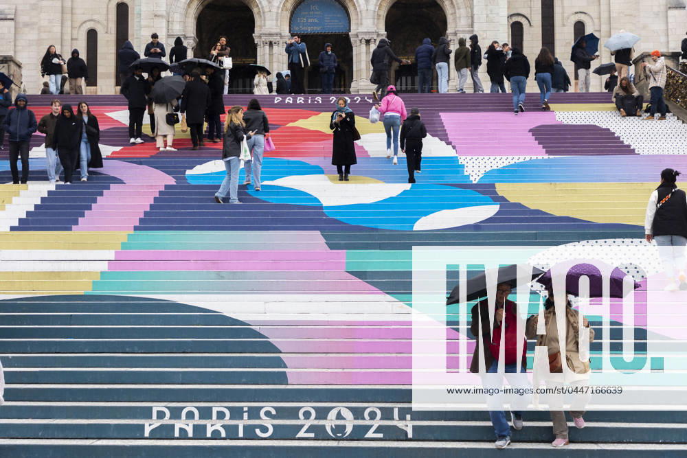 Paris, France April 19, 2024 - People walk up the stairs leading to the Sacre Coeur basilica decorated with a fresco in Olympic colors as part of the preparations for the Paris 2024 Olympic Games. Less than 100 days remain for the Olympic and Paralympic Games organizers to finalize preparations for the event that will welcome millions of visitors from July 16. OLY, JEUX OLYMPIQUES PARIS 2024, DECORATIONS, FRESQUE, ILLUSTRATION, MONTMARTRE, BASILIQUE DU SACRE COEUR, SPORT, ESCALIERS, MARCHES COLOREES,