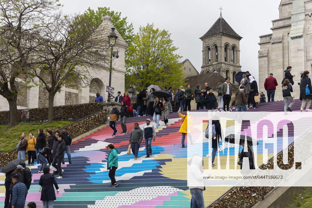 Paris, France April 19, 2024 - People walk up the stairs leading to the Sacre Coeur basilica decorated with a fresco in Olympic colors as part of the preparations for the Paris 2024 Olympic Games. Less than 100 days remain for the Olympic and Paralympic Games organizers to finalize preparations for the event that will welcome millions of visitors from July 16. OLY, JEUX OLYMPIQUES PARIS 2024, DECORATIONS, FRESQUE, ILLUSTRATION, MONTMARTRE, BASILIQUE DU SACRE COEUR, SPORT, ESCALIERS, MARCHES COLOREES,