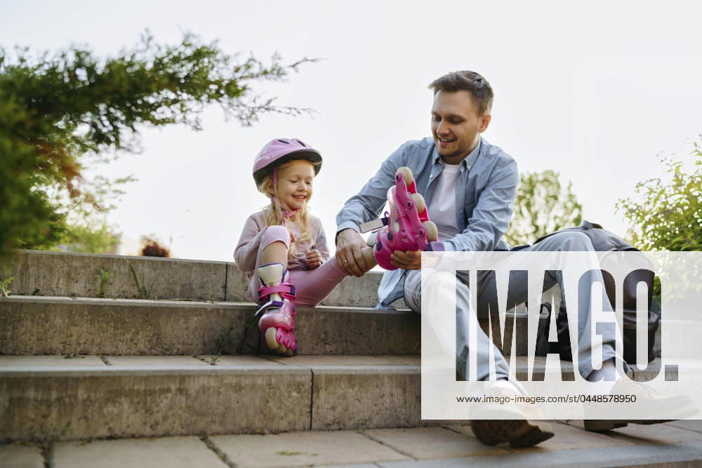 Smiling man helping daughter to wear roller skates sitting on steps model released, Symbolfoto, NSTF00054