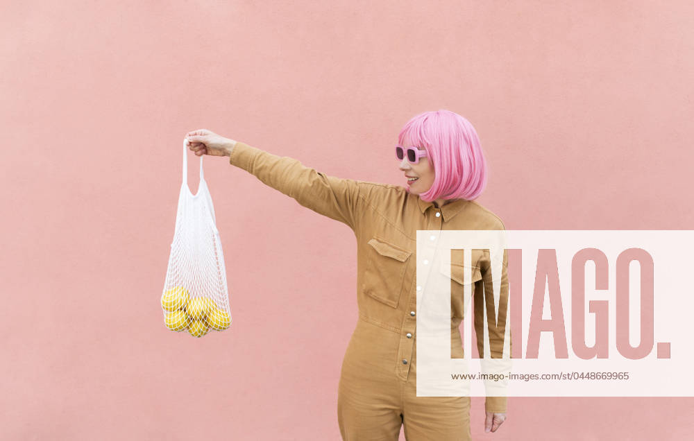 Smiling woman holding mesh bag with lemons in front of pink wall model released, Symbolfoto, VRAF00503