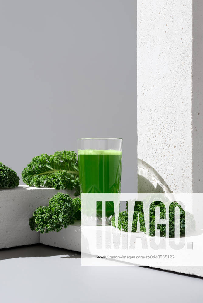 A transparent glass filled with vibrant green kale juice is placed next to fresh, crisp kale leaves on a modern white surface, showcasing a healthful drink option Model Released RuthCarrodeguas_ID21186_624725_005