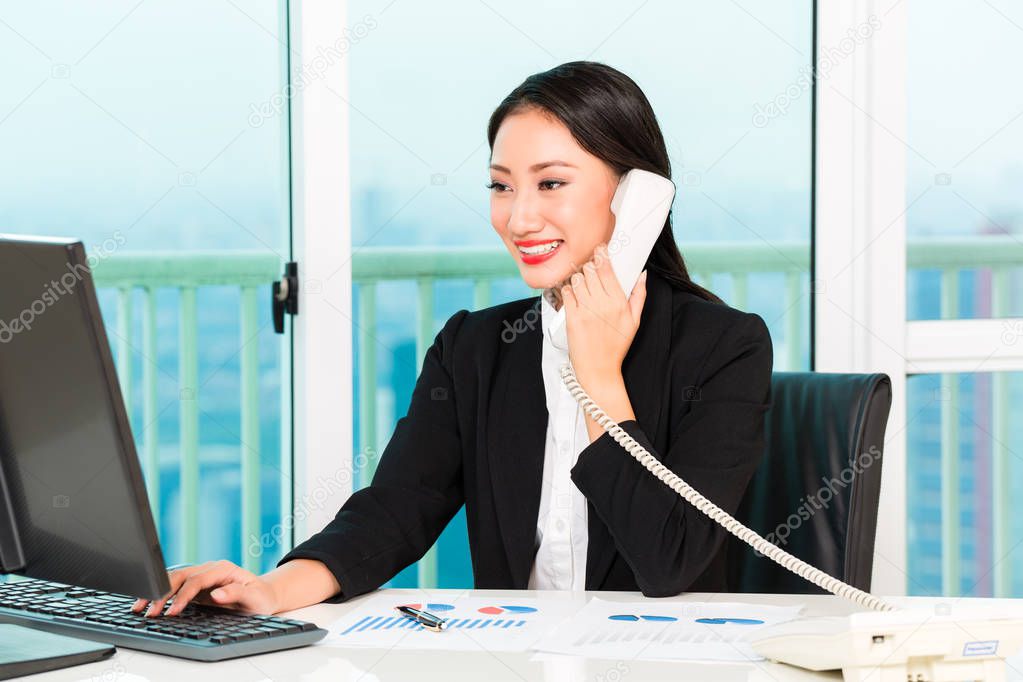 Close-up of smiling businesswoman talking on telephone looking at computer in the office model released