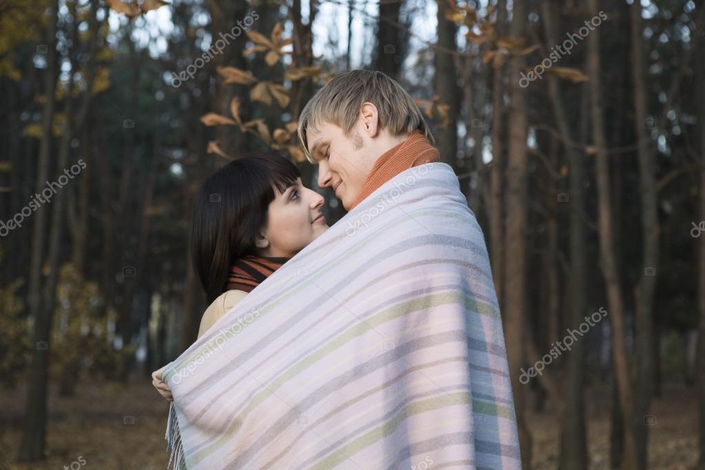 Young couple wrapped in blanket embracing in forest model released