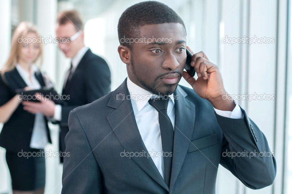 Closeup of smiling businessman talking on cellphone with colleagues in the background. model released