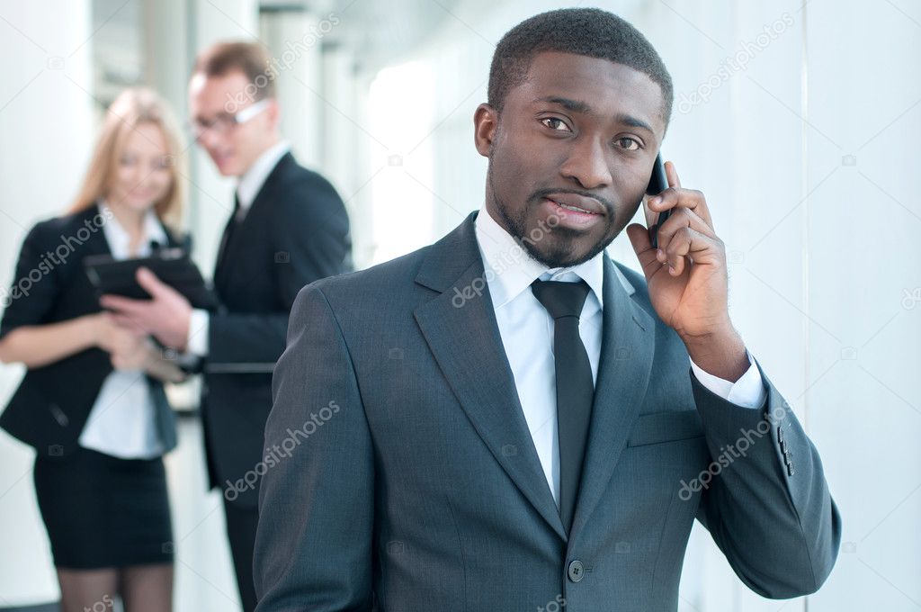 Closeup of smiling businessman talking on cellphone with colleagues in the background. model released