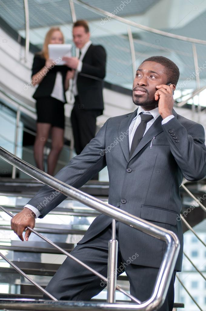 Closeup of smiling businessman talking on cellphone with colleagues in the background. model released