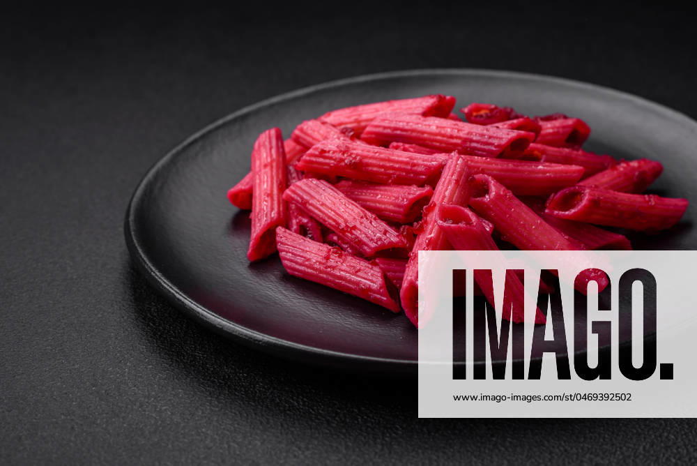 Delicious penne pasta with beets, cheese, salt and spices Delicious penne pasta with beets, cheese, salt and spices on a dark concrete background