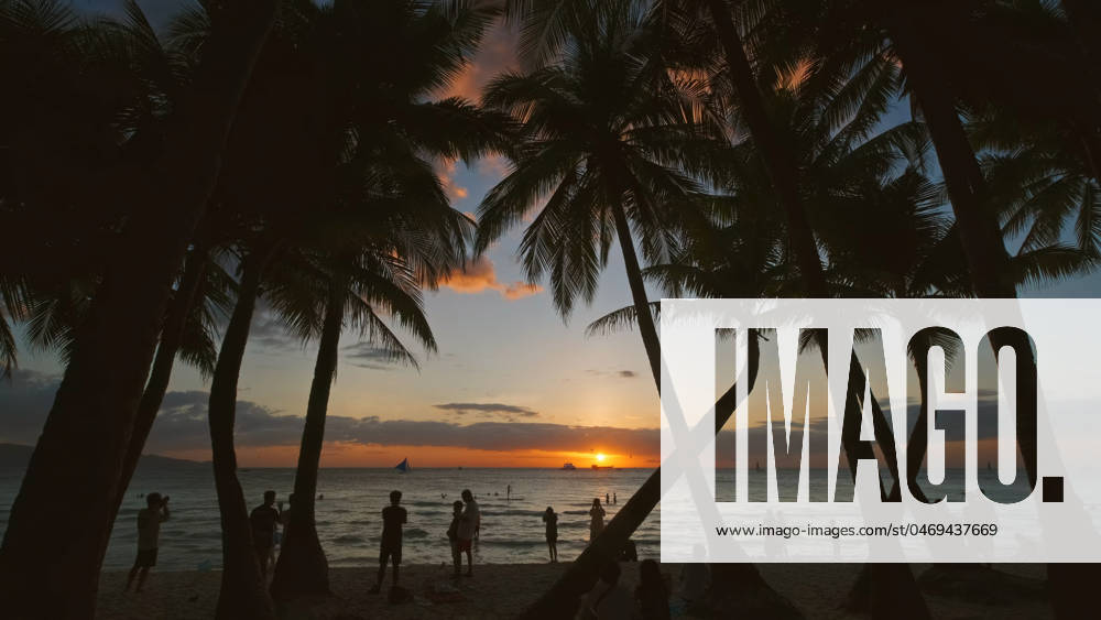 Sunset on beach with people and palms Silhouetted people and palms near sea. Sunset at tropical White beach, Boracay island, Philippines