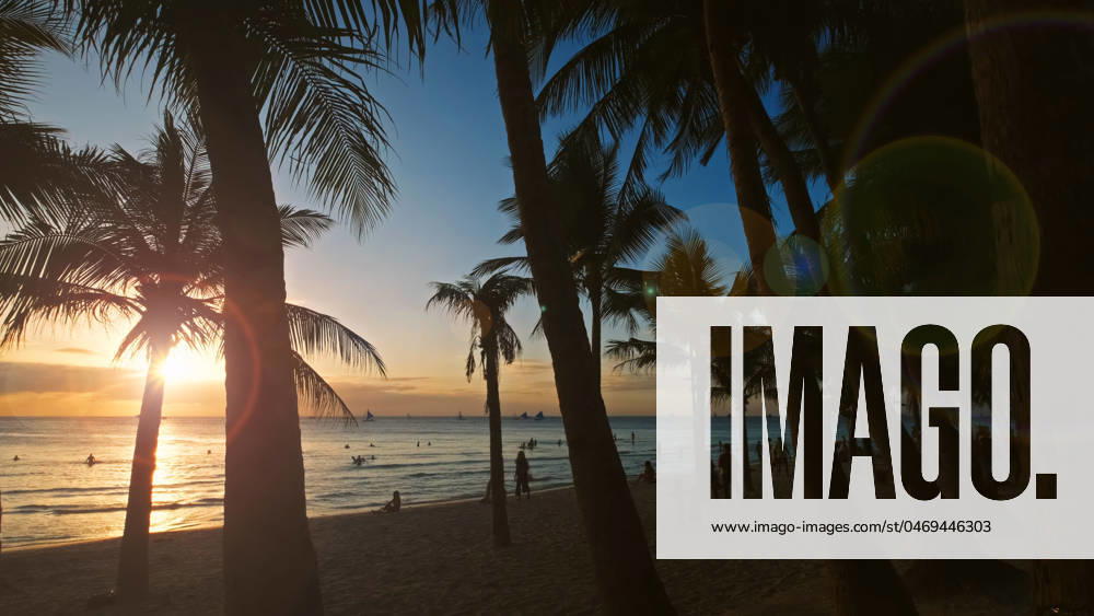 Sunset on beach with people and palms Silhouetted people and palms near sea. Sunset at tropical White beach, Boracay island, Philippines