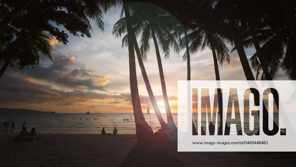 Sunset on beach with people and palms Silhouetted people and palms near sea. Sunset at tropical White beach, Boracay island, Philippines