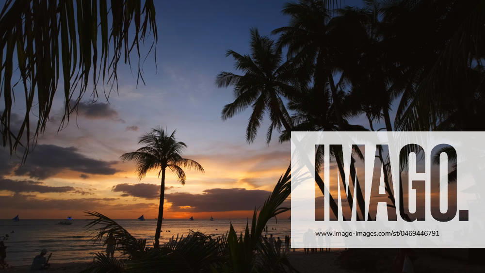 Sunset on beach with people and palms Silhouetted people and palms near sea. Sunset at tropical White beach, Boracay island, Philippines