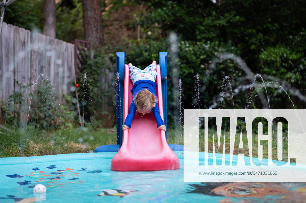 IMAGO Creative, Sommer, Sommertage im Garten Young boy slides headfirst down toddler slide into splah pad. Atlanta, Georgia, United States R_PJUI240426-1406671-01 ,model released, Symbolfoto